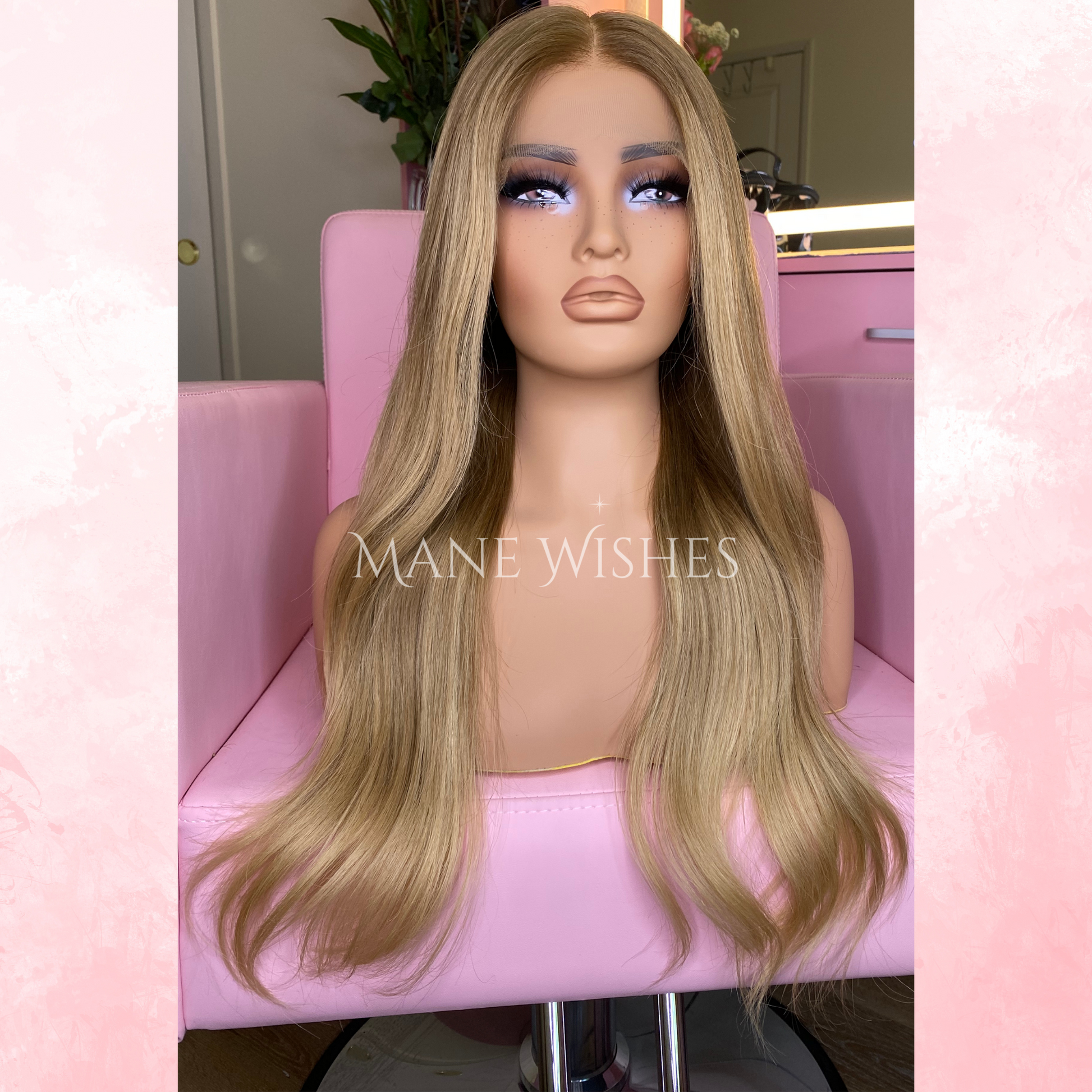 Blonde wig on a mannequin head with 'Mane Wishes' branding, seated on a pink chair.