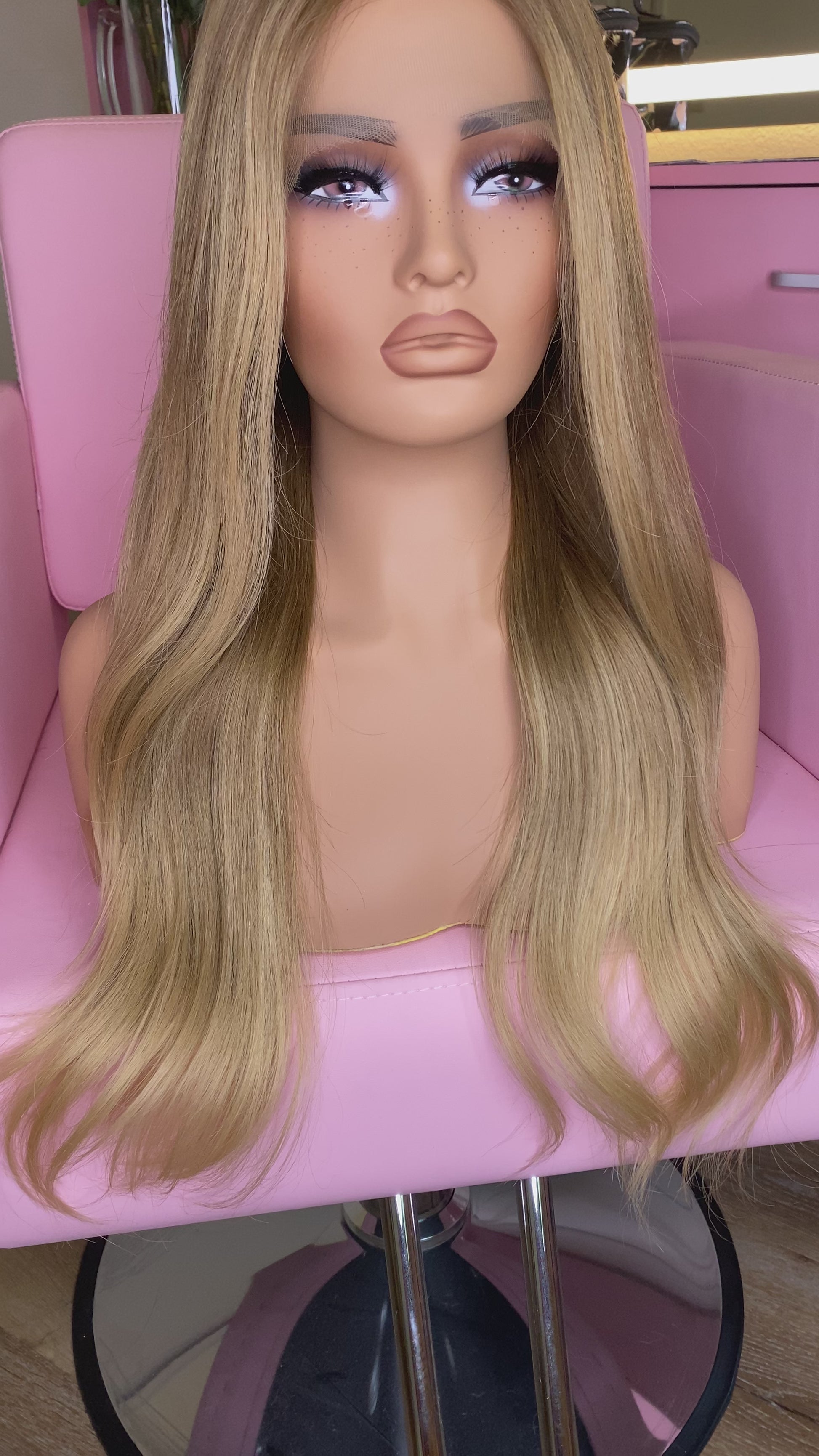 Blonde wig on a mannequin head with 'Mane Wishes' branding, seated on a pink chair.