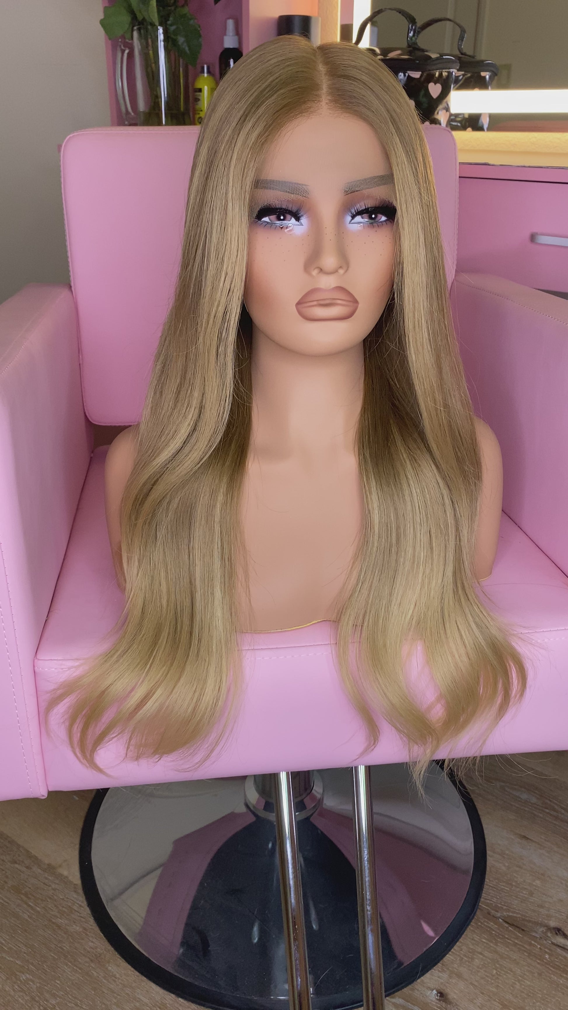 Blonde wig on a mannequin head with 'Mane Wishes' branding, seated on a pink chair.