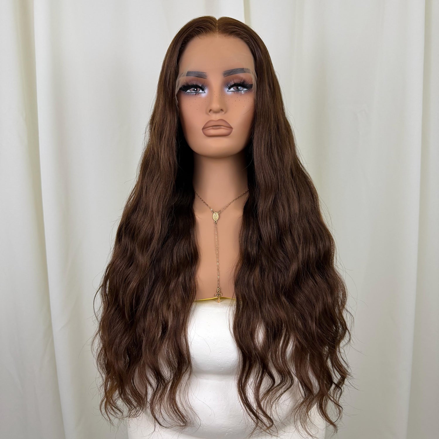 Mannequin head with long brown wavy wig against a white curtain background