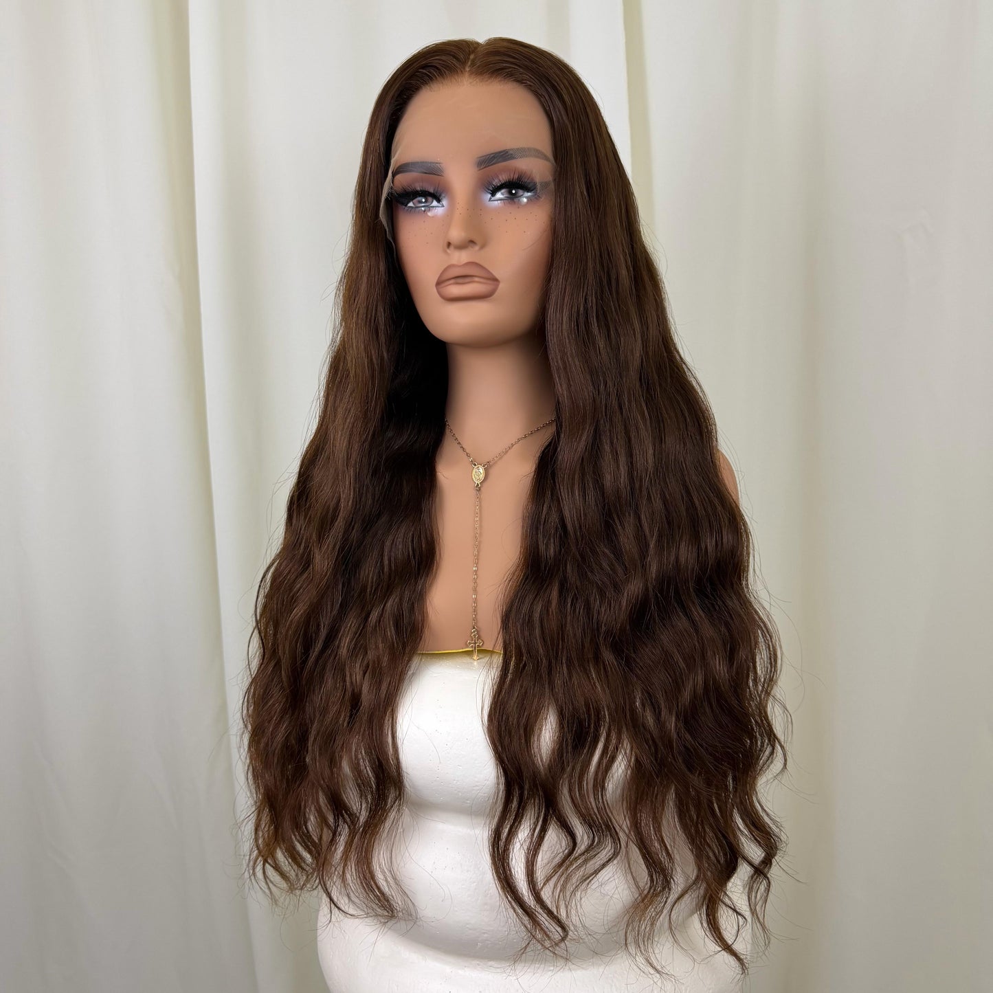 Mannequin head with long brown wig against a white curtain background