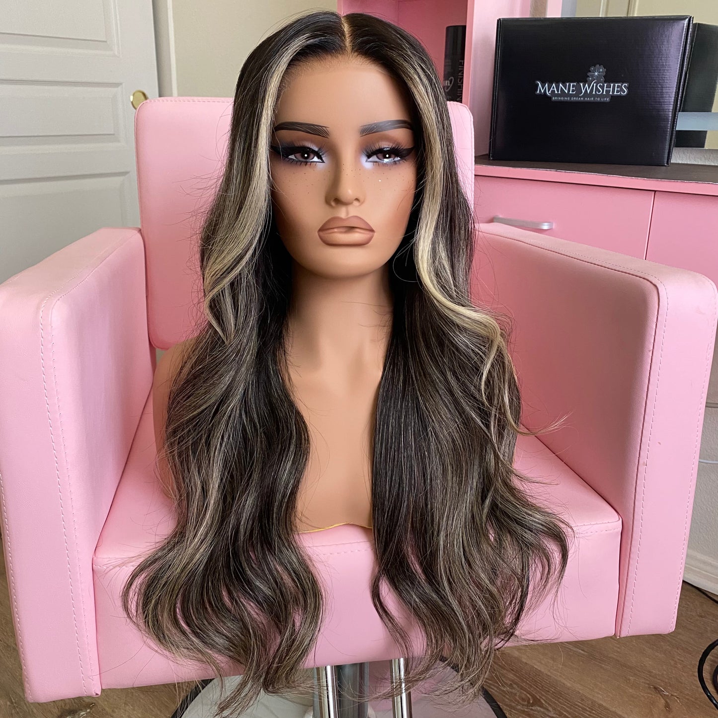 Mannequin head with long, wavy wig on a pink chair, with 'Mane Wishes' branding in the background.
