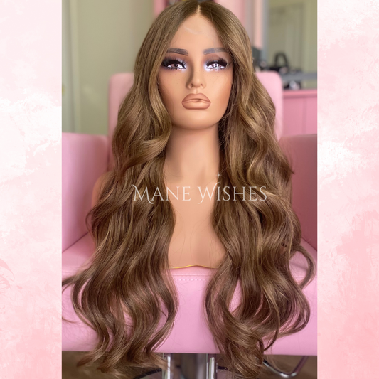 Mannequin head with long, wavy brown wig on a pink chair, branded 'Mane Wishes'.