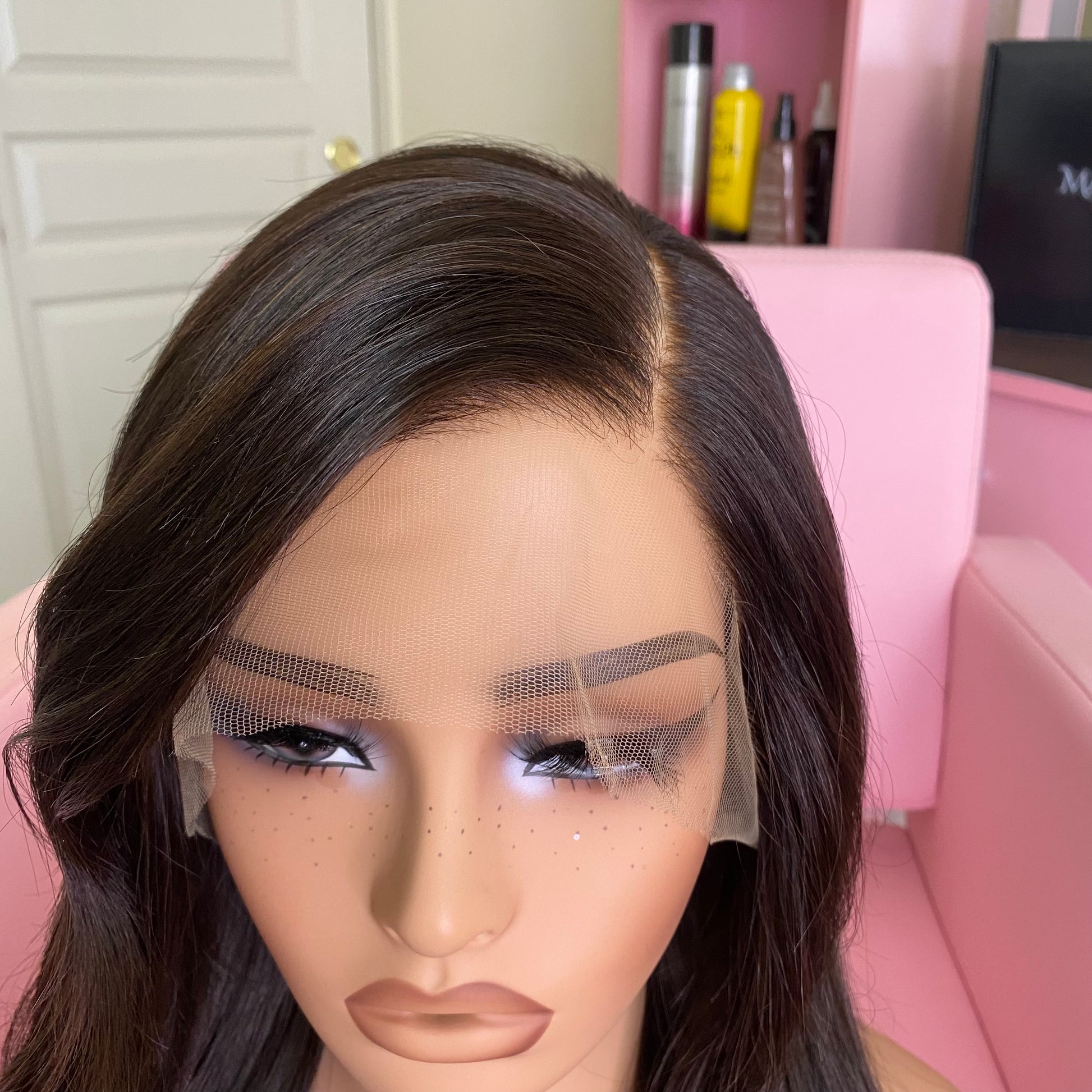 Mannequin head with a wig and makeup on a pink chair.