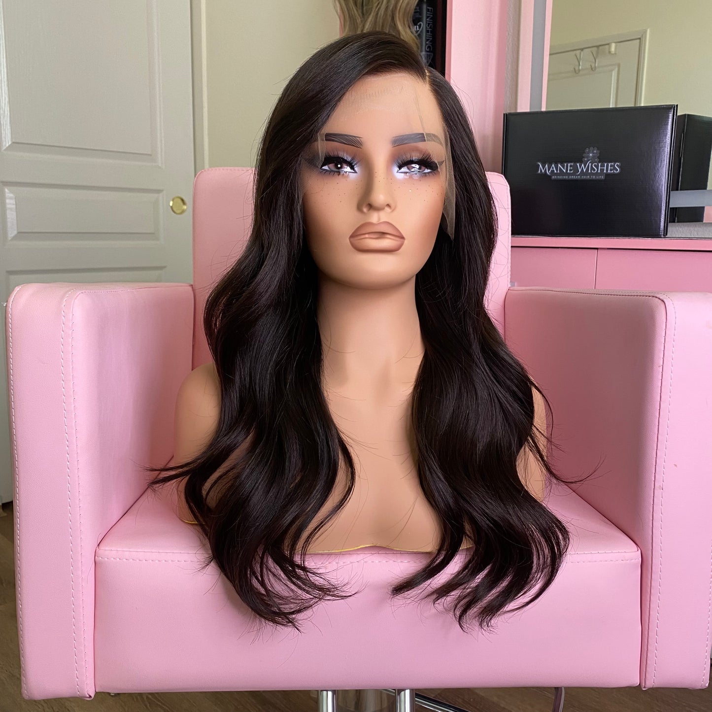 Mannequin head with long black wig on a pink chair, with 'Mane Wishes' branding in the background.