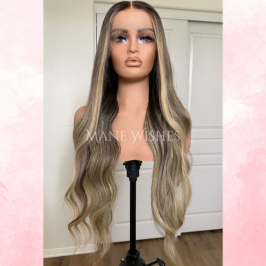 Mannequin head with long, wavy blonde wig on a stand against a white wall
