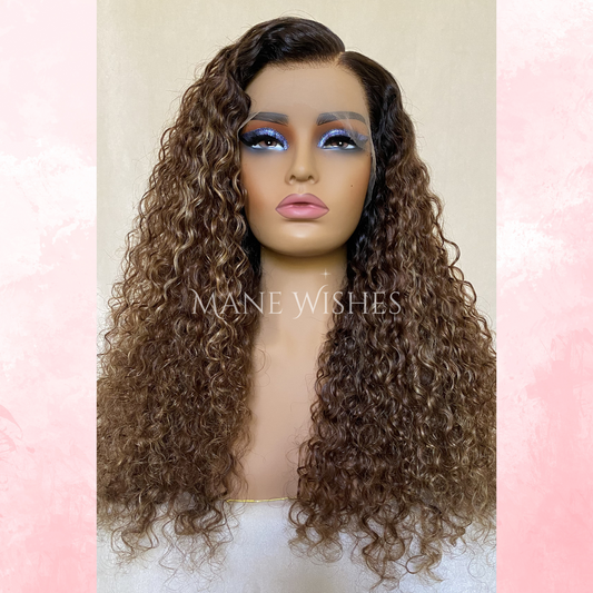 Mannequin head with curly brown wig on a pastel pink and beige background, featuring the brand 'Mane Wishes'.