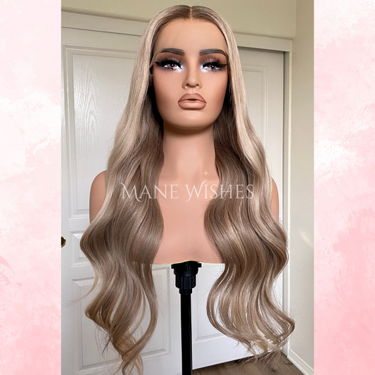 Blonde wig on a mannequin head with 'Mane Wishes' branding against a white door background.