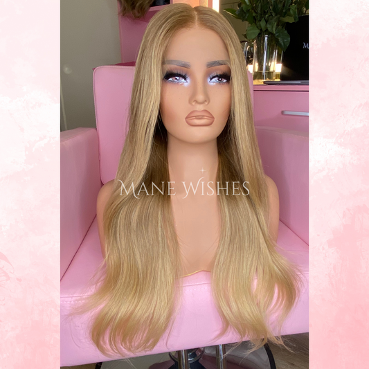 Blonde wig on a mannequin head with 'Mane Wishes' branding, set against a pink background.