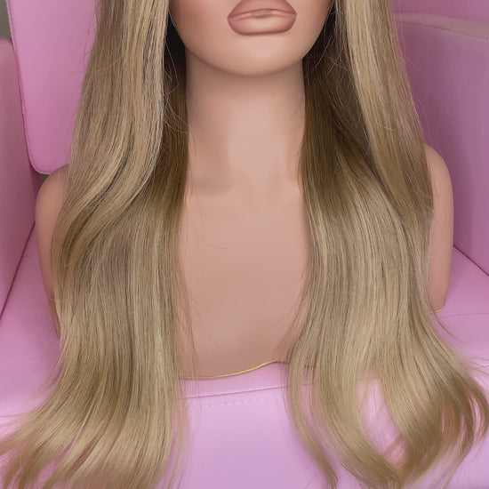 Blonde wig on a mannequin head with 'Mane Wishes' branding, seated on a pink chair.