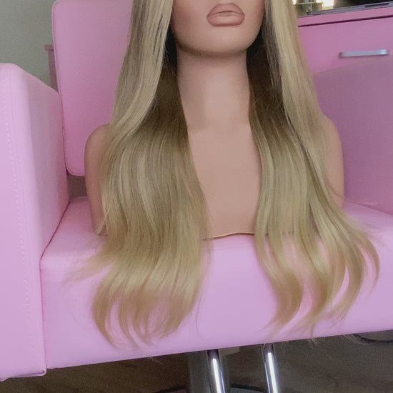 Blonde wig on a mannequin head with 'Mane Wishes' branding, seated on a pink chair.