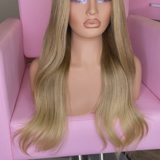 Blonde wig on a mannequin head with 'Mane Wishes' branding, seated on a pink chair.